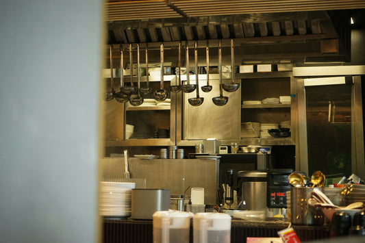 Peering into a restaurant's kitchen with soup ladles hung up and stainless steel cabinets in the background